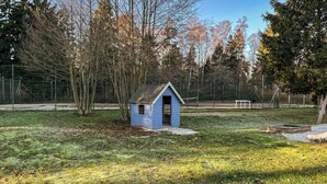 Een klein blauw tuinhuisje in een grasrijke omgeving met bomen en een hek op de achtergrond.