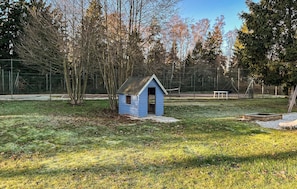Ein kleines blaues Gartenhaus auf einer Wiese, im Hintergrund Bäume und ein Zaun.