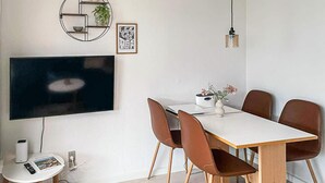 Een eetgedeelte met een aan de muur bevestigde televisie, een rond schap met een plant en een ingelijste foto.