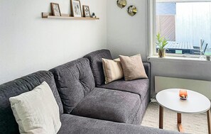 A living room with a grey sofa, a small round table, and a window with a view. - Beautiful apartment in Nexø with sauna (Nexø)
