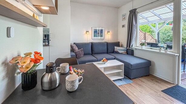 En moderne stue med en hjørnesofa, et sofabord og et spisebord med elkedel og kopper.