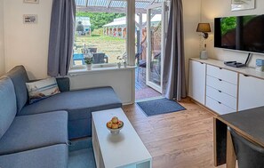 Ein modernes Wohnzimmer mit einer Couch, einem Couchtisch mit Obst, einem Fernseher und Blick ins Freie.