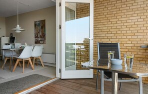 A modern dining area with a glass table, white chairs, and a brick wall. - Cozy apartment in Allinge with WiFi (Allinge)