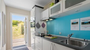 A modern kitchen with white cabinets, a blue accent wall, and a stainless steel sink. - Cozy apartment in Allinge with WiFi (Allinge)
