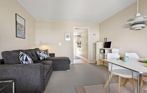 Ein modernes Wohnzimmer mit einem grauen Sofa, einem Esstisch mit Stühlen und einer Küchenzeile im Hintergrund.