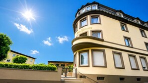 A corner building with a curved facade, a visible entrance with a gate, and a clear sky. - Zum Rheinberg – Balcony Suite (Braubach)