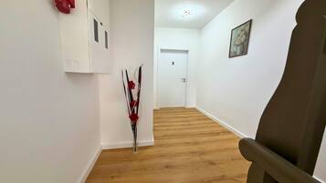 A hallway with wooden flooring, a white door marked with the number 5, and a vase with red flowers.