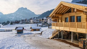 Un chalet de madera con balcón que da a un paisaje nevado y una montaña al fondo.