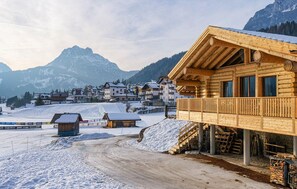 Eine Holzchalet mit einem Balkon mit Blick auf eine verschneite Landschaft und einem Berg im Hintergrund.