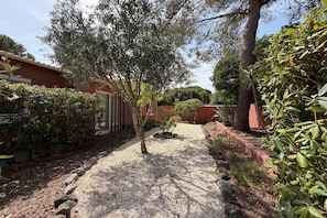 A pathway leading to a building with a red exterior, surrounded by various shrubs and trees. - Charming Villa for 6 in Agde (Agde)