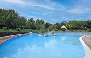 Ein Swimmingpool mit einer umlaufenden Ziegelterrasse, Bäumen und einem weißen Gazebo im Hintergrund.