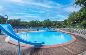 Una piscina con un tobogán azul, rodeada por una terraza de madera y un muro de piedra.
