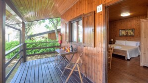Una cabaña de madera con un balcón, un comedor con mesa y sillas, y un dormitorio con cama y un cuadro en la pared.
