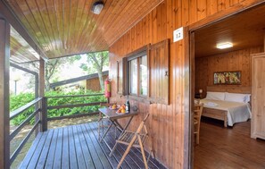 Eine Holzhütte mit einem Balkon, einem Essbereich mit Tisch und Stühlen sowie einem Schlafzimmer mit einem Bett und einem Bild an der Wand.