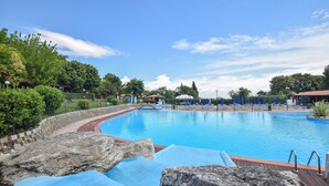 Una piscina con cubierta de madera, sillas de descanso y sombrillas.