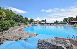 A swimming pool with a wooden deck, lounge chairs, and umbrellas.