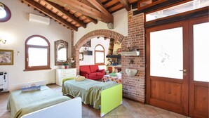 Quarto com duas camas, uma cadeira vermelha, lareira de tijolos e porta de madeira.