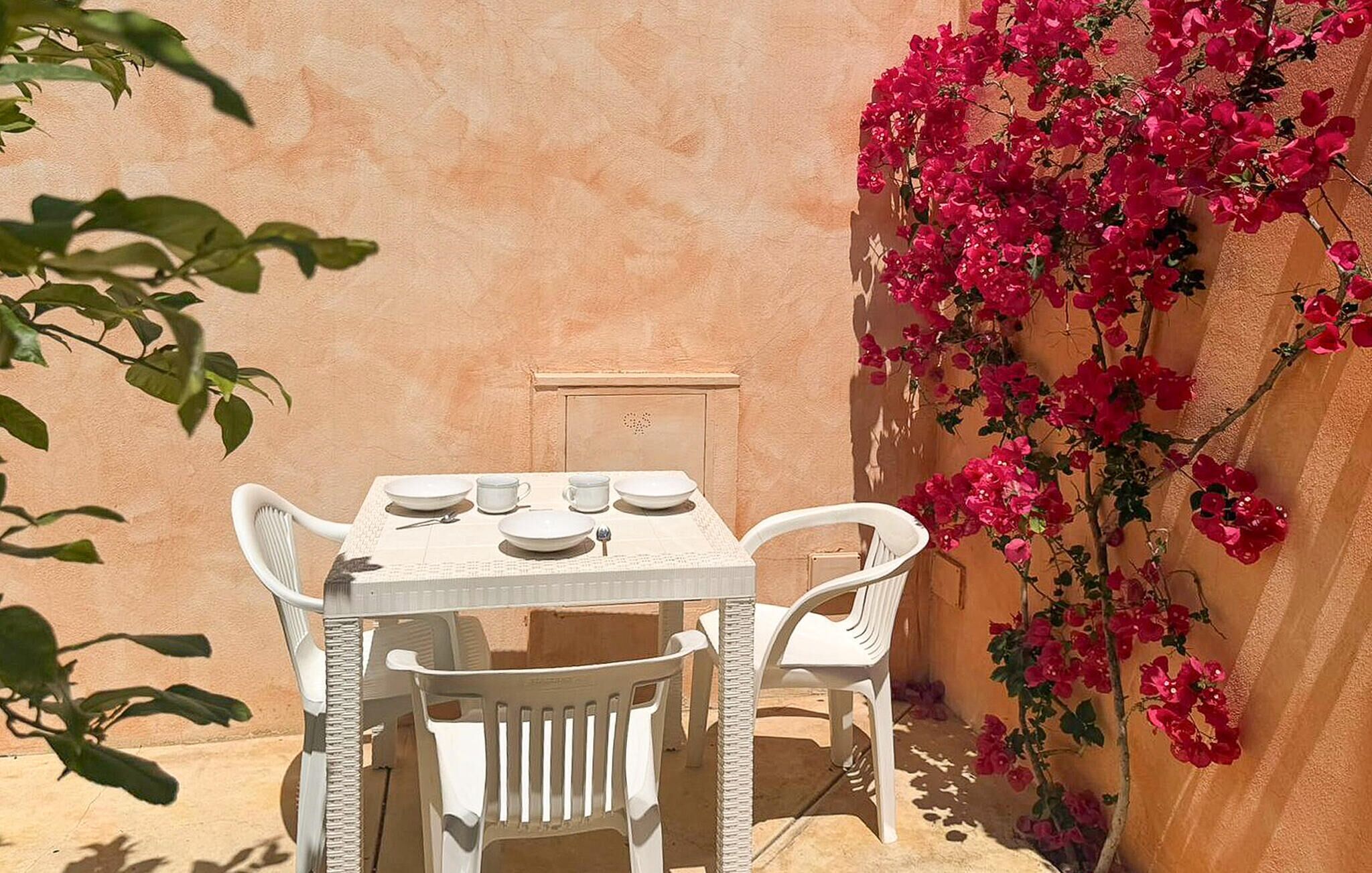 Une table blanche avec quatre chaises, un petit meuble blanc et un mur recouvert de fleurs roses.