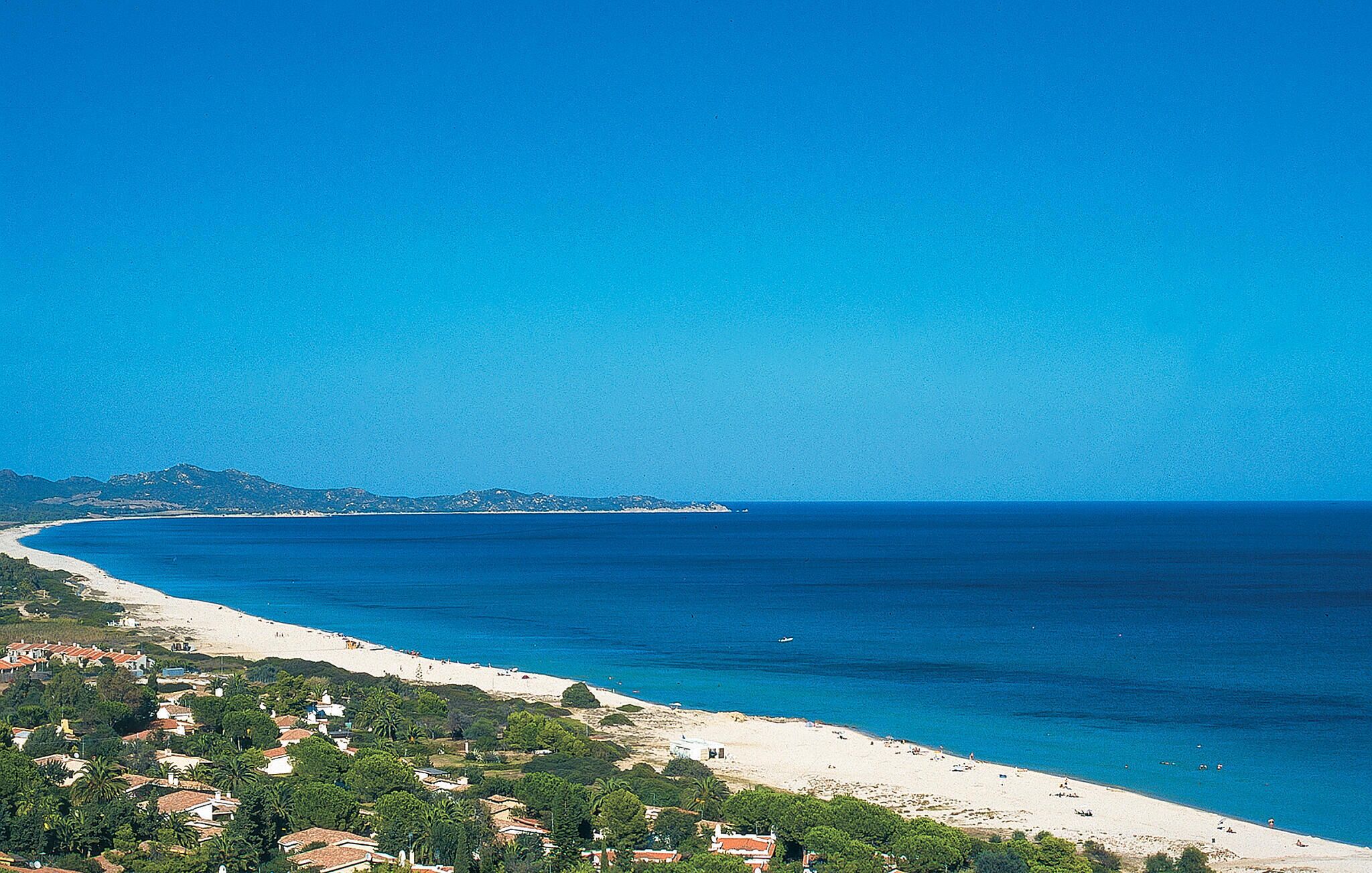 Blick auf die Küste mit Strand, blauem Himmel und fernen Bergen.