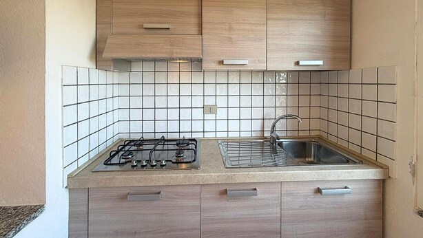 A kitchen with a gas stove, a sink, and wooden cabinets. - Stunning home in Costa Rei with WiFi (Costa Rei)