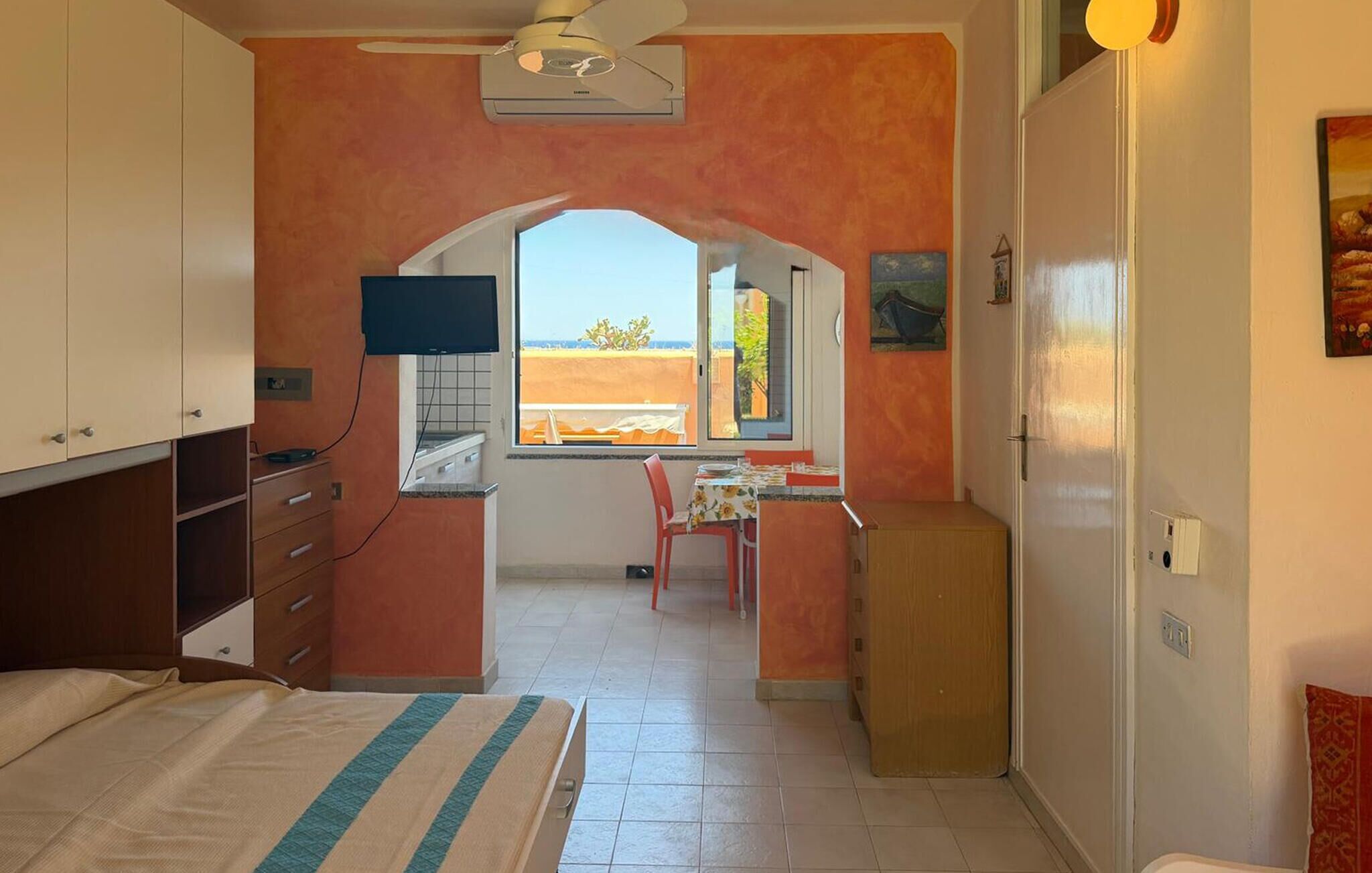 Een kamer met een bed, een bureau en stoel, een kleine kitchenette en een raam met uitzicht.
