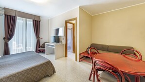 Et hotelværelse med en seng, et skrivebord med computer, et fjernsyn, en sofa og et spisebord med stole.