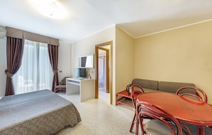 Ein Hotelzimmer mit Bett, Schreibtisch mit Computer, Fernseher, Sofa und Esstisch mit Stühlen.
