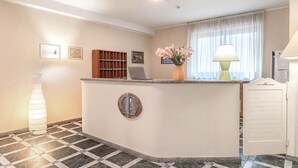 En reception med et skrankeområde, et bord, en stol, en vase med blomster, en lampe og en dør.