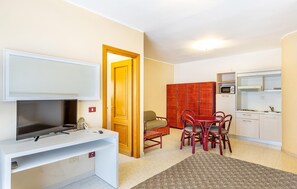 Ein gemütlicher, kleiner Wohnraum mit Fernseher, Küchenzeile, Essbereich und einer Tür zu einem weiteren Zimmer.