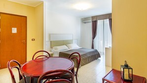 Ein Hotelzimmer mit Bett, Nachttisch, kleinem Tisch mit Stühlen, Lampe und Tür.