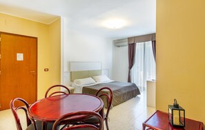 Ein Hotelzimmer mit Bett, Nachttisch, kleinem Tisch mit Stühlen, Lampe und Tür.