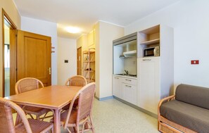 Eine kleine Küche mit einer Mikrowelle, einem Spülbecken und einem Schrank. Ein Esstisch mit Korbstühlen und ein Sofa sind ebenfalls vorhanden.