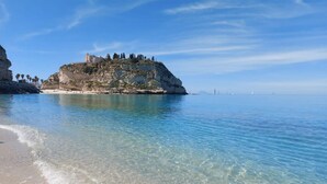 A coastal landscape with clear waters, a sandy beach, and a rocky outcrop with a building on top. - Lovely apartment in Tropea with WiFi (Tropea)
