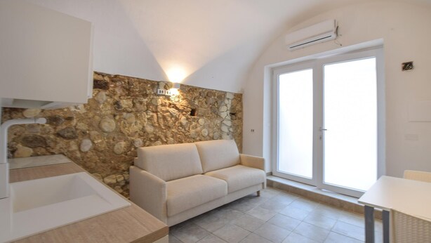 A modern kitchen with a stone wall, a sofa, and a large window. - Lovely apartment in Tropea with WiFi (Tropea)
