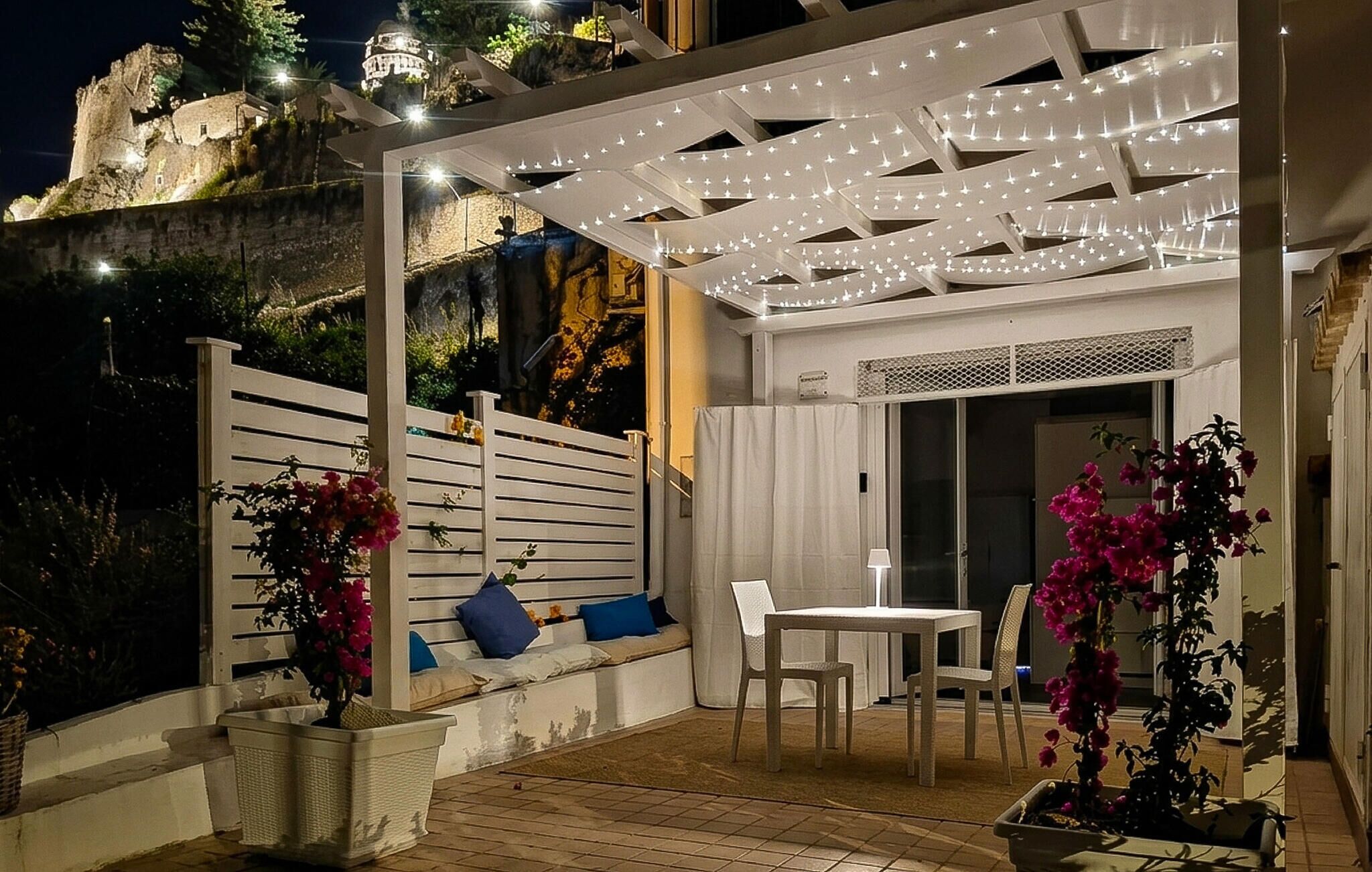 A patio with a table and chairs, a covered seating area with cushions, and a view of a historic building in the background.