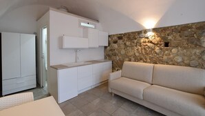 A compact living space with a kitchenette, a stone accent wall, and a sofa. - Lovely apartment in Tropea with WiFi (Tropea)