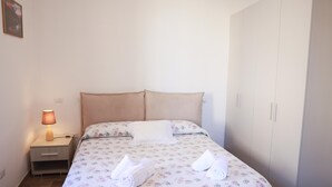 Una cama bien tendida con ropa de cama floral, dos almohadas y dos toallas enrolladas.