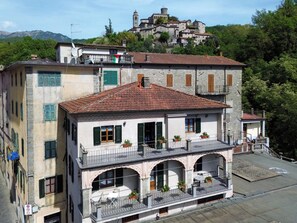 A multi-story building with balconies, a stone facade, and a view of a hilltop castle.