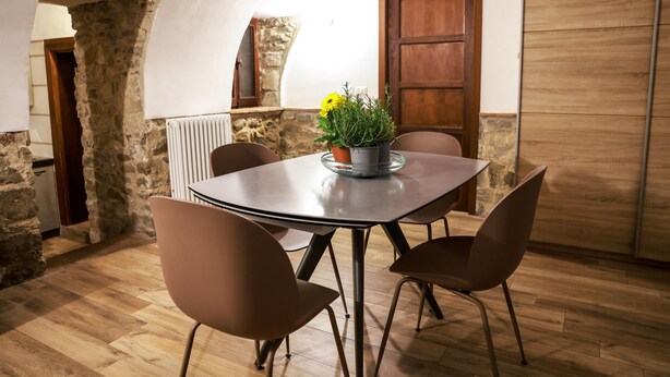 Un comedor con una mesa y sillas, una planta en maceta con flores amarillas y una pared de piedra.