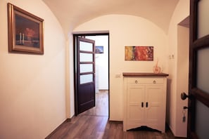 A hallway with a wooden floor, a white cabinet with two doors, a painting on the wall, and a door leading to another room.