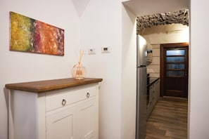 A hallway with a white cabinet, a painting on the wall, and a kitchen area with a wooden door.