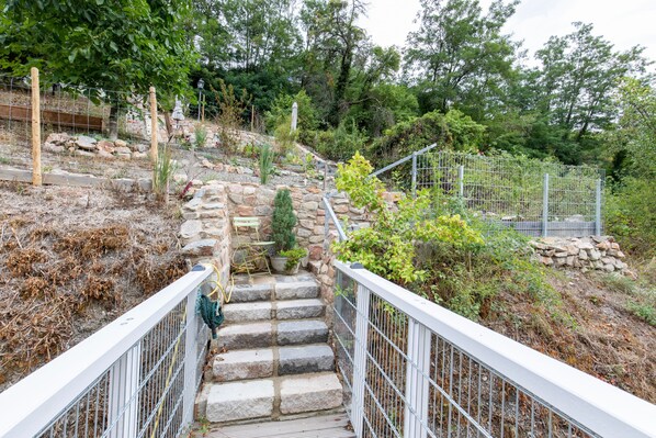 A stone staircase with metal railings leading up to a garden area with various plants and a small tree.