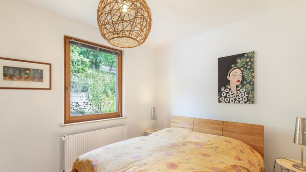 A bedroom with a bed, a window, a radiator, a wall-mounted light, and a painting. - Holiday Home 'Hiwwelhaus' with Private Terrace, Private Garden and Wi-Fi (Oberdiebach)