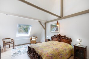 Un dormitorio con una cama grande, una ventana, una silla, una mesita y una lámpara.