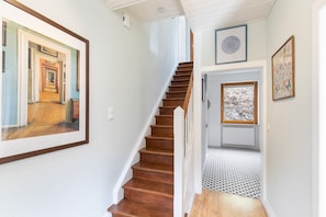 A staircase with wooden steps leading to a landing, a white wall with a framed picture, and a door with a window.