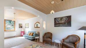 A spacious living room with a wooden ceiling, a blue sofa, two armchairs, a small white table, and a patterned rug. - Holiday Home 'Hiwwelhaus' with Private Terrace, Private Garden and Wi-Fi (Oberdiebach)