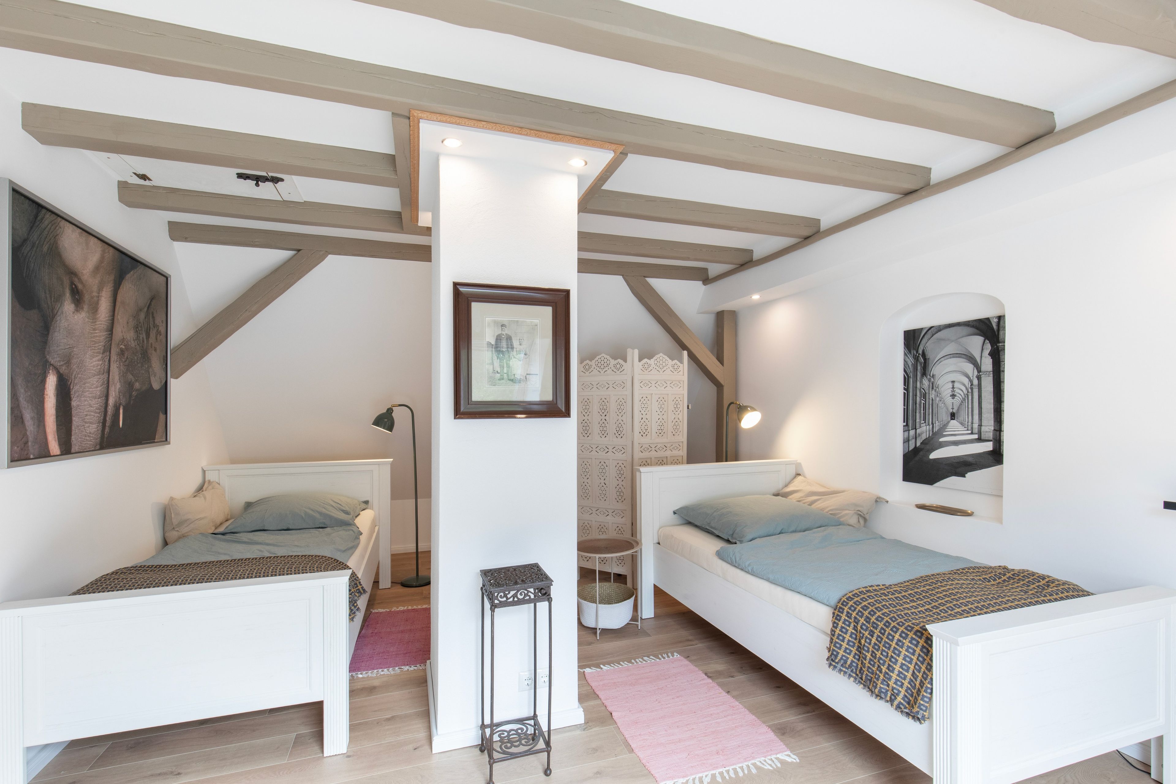 A bedroom with two single beds, a standing lamp, and a framed picture on the wall.
