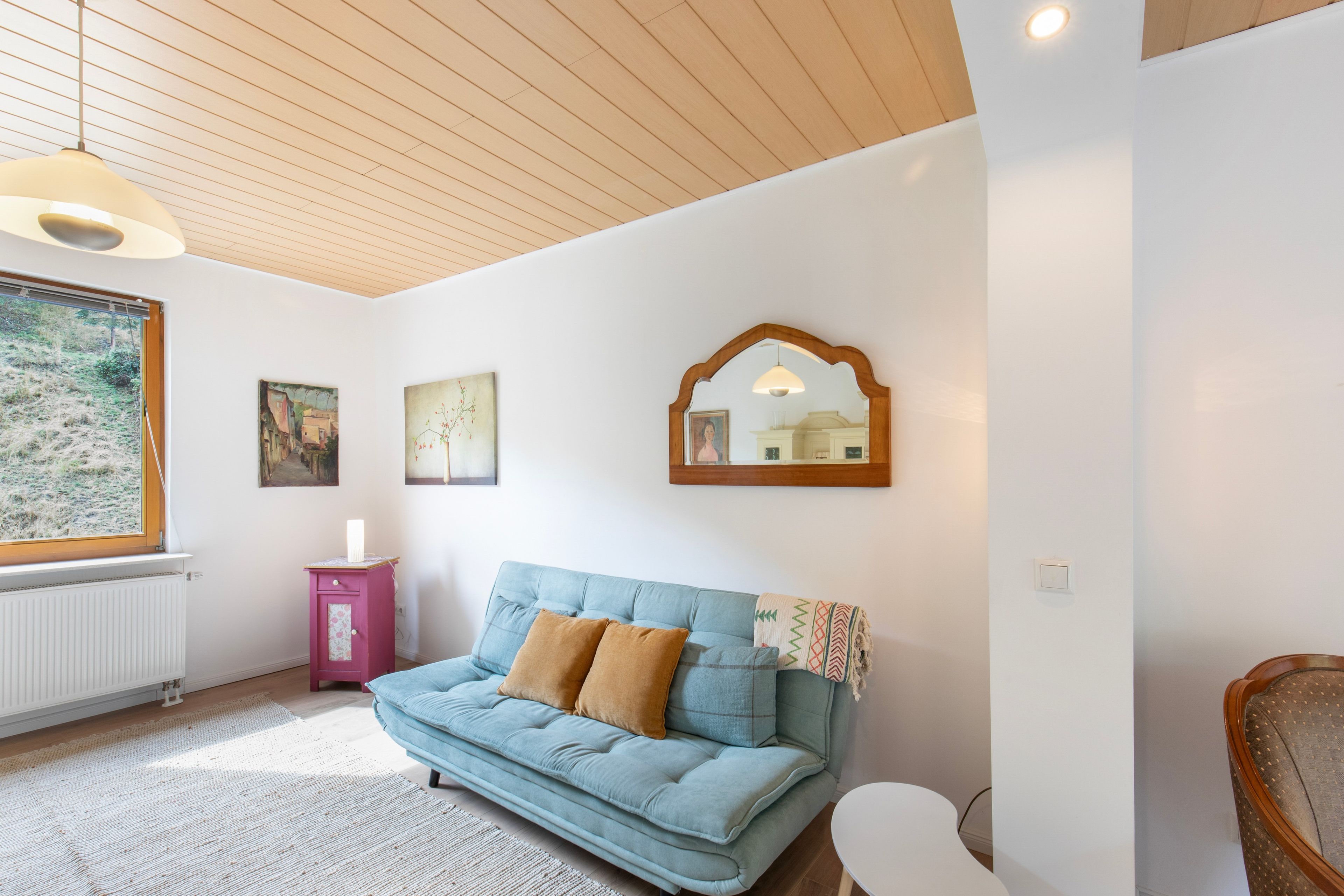 A room with a blue sofa, a pink cabinet, and a large window.