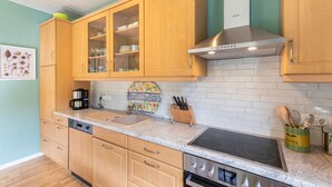 A kitchen with wooden cabinets, a stainless steel range hood, a built-in oven, and a countertop with a coffee maker and a knife block. - Holiday Home 'Hiwwelhaus' with Private Terrace, Private Garden and Wi-Fi (Oberdiebach)