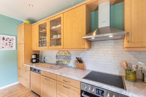 A kitchen with wooden cabinets, a stainless steel range hood, a built-in oven, and a countertop with a coffee maker and a knife block.